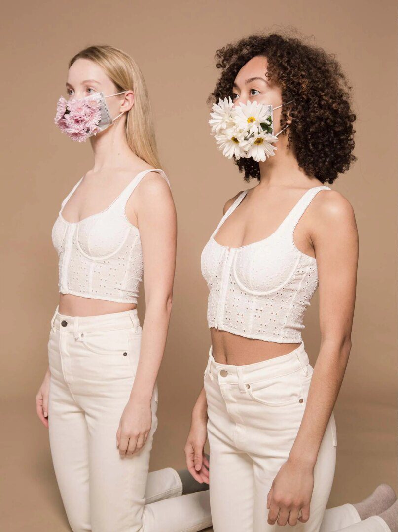 Two women wearing white shirts and a floral mask.