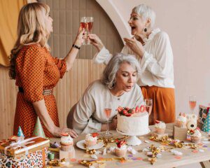 Three women are celebrating a birthday with cake and champagne.