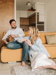 A man and woman sitting on the couch with their cat.