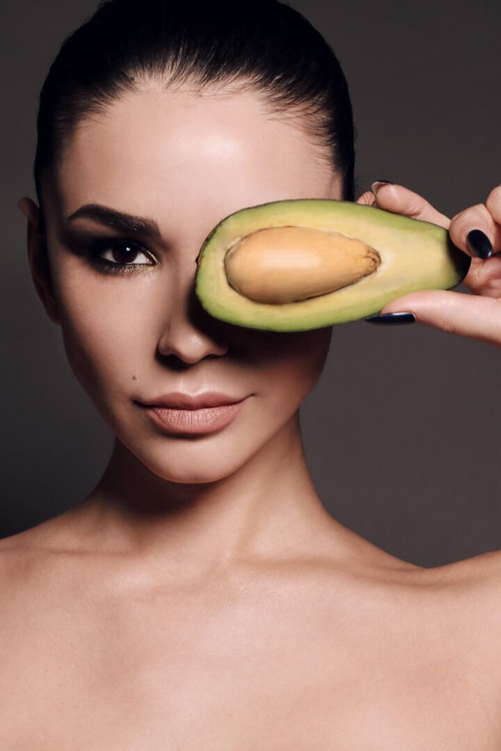 A woman holding an avocado in front of her eye.