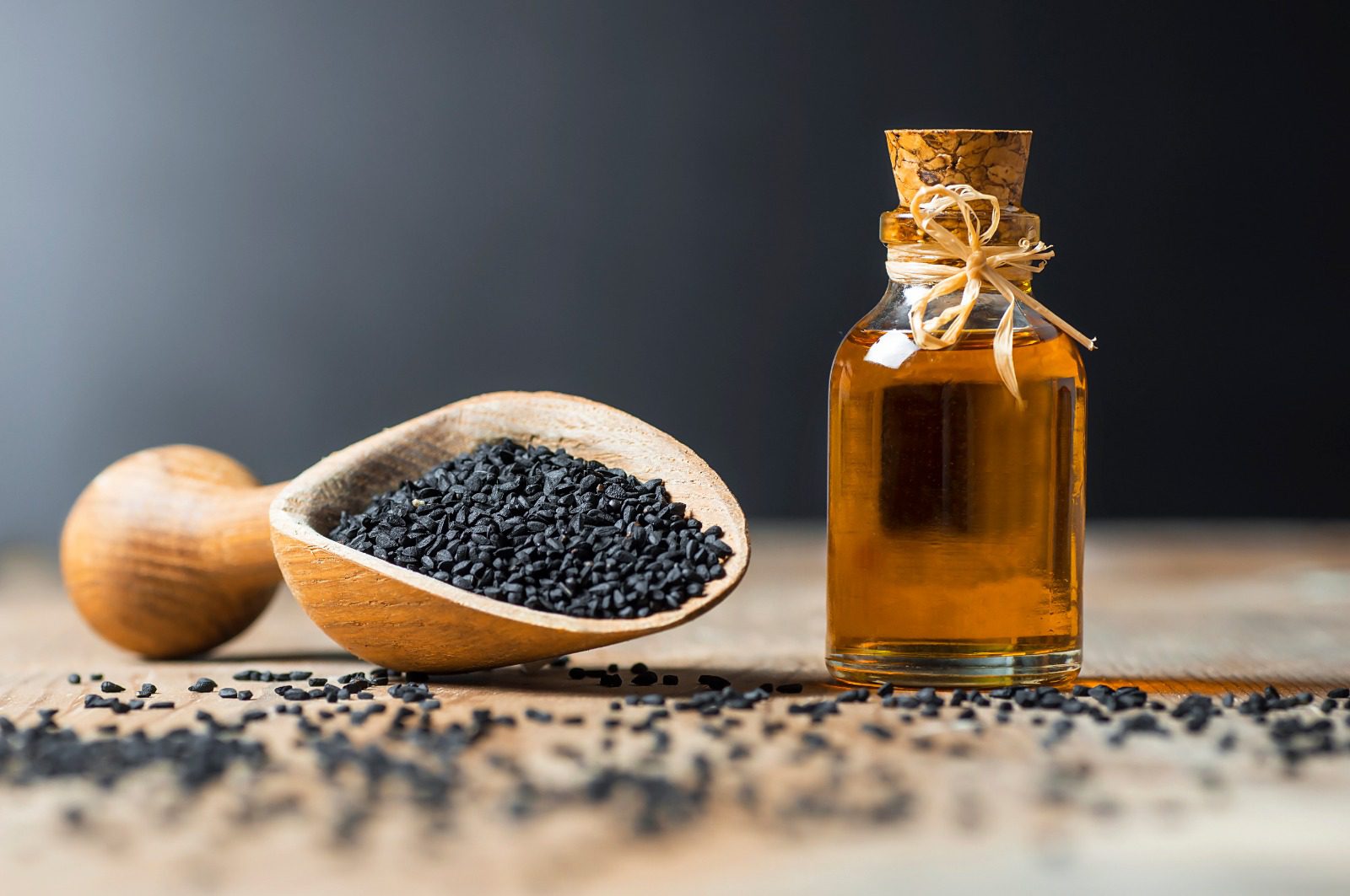 A wooden bowl of black seeds next to a bottle of oil.