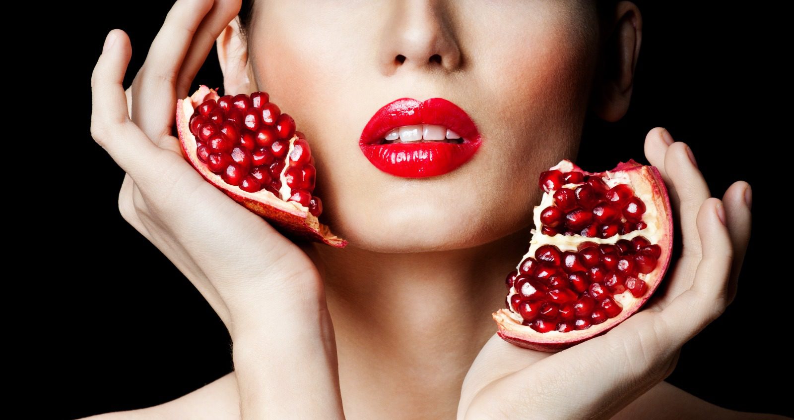 A woman with red lipstick holding two pieces of fruit.