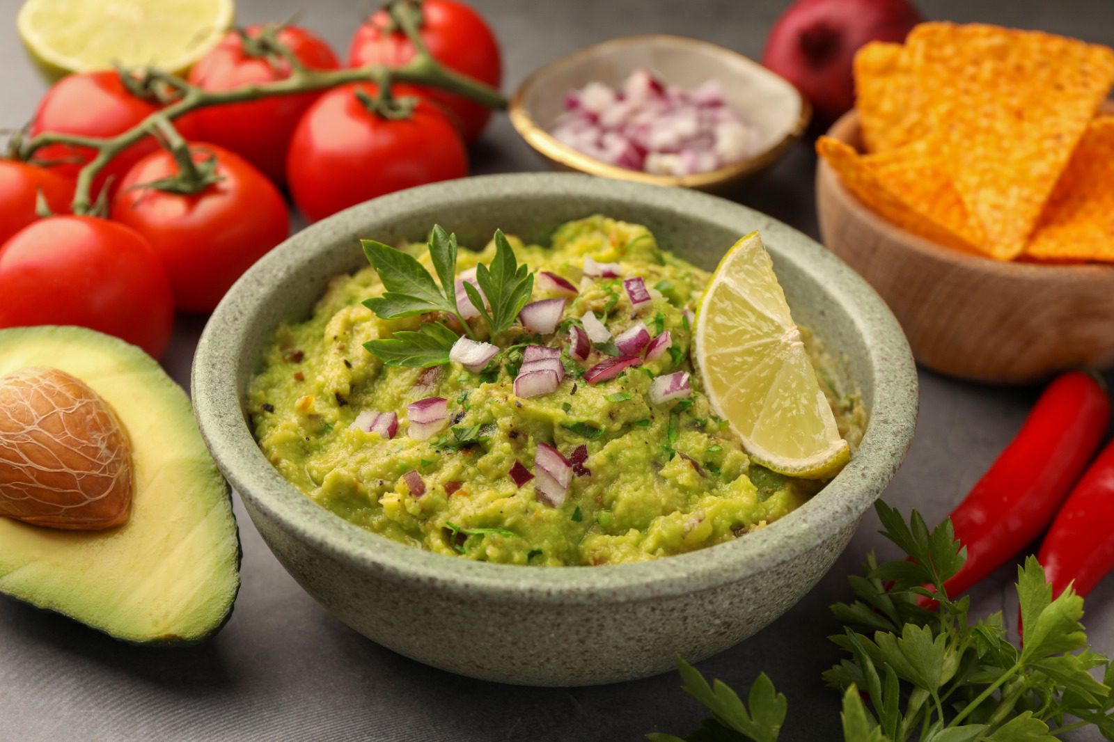 A bowl of guacamole with ingredients in the background.