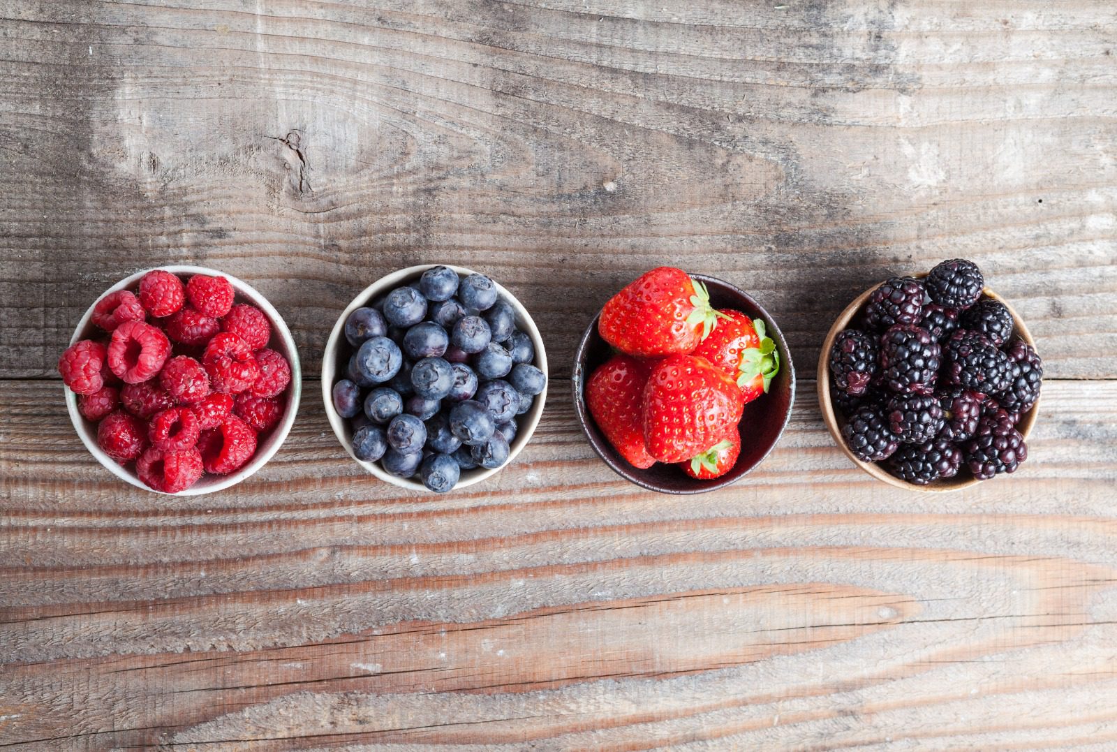 Four bowls of berries are lined up on a table.