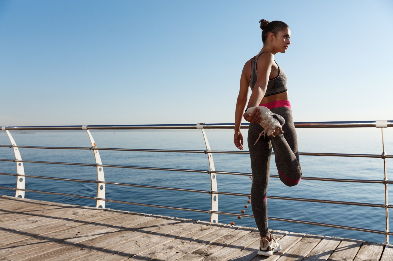 A woman is stretching on the pier by the water.