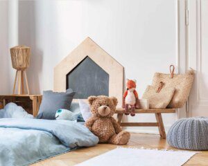 A teddy bear sitting on the floor in front of a bed.