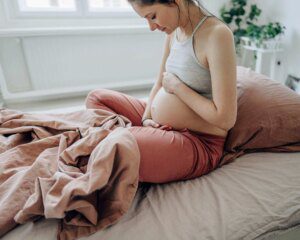 A pregnant woman sitting on the bed with her stomach in her hands.