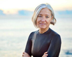 A woman in a black wetsuit standing on the beach.