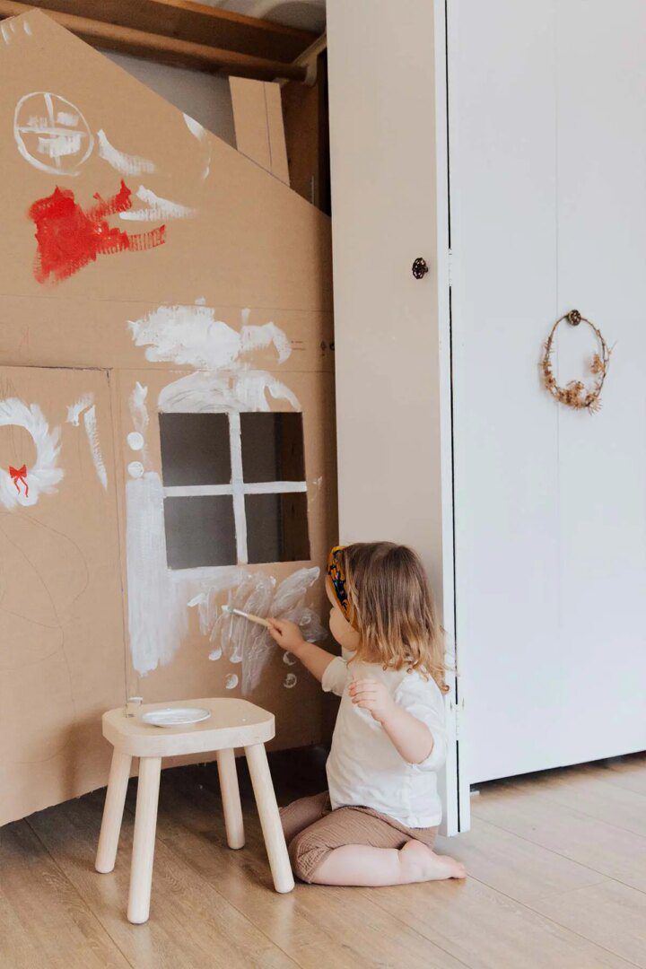 A little girl painting a house with white paint.