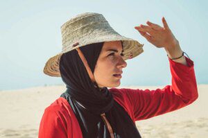 A woman in a hat and scarf on the beach.