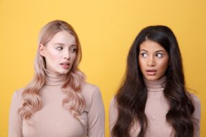 Two women standing next to each other in front of a yellow wall.