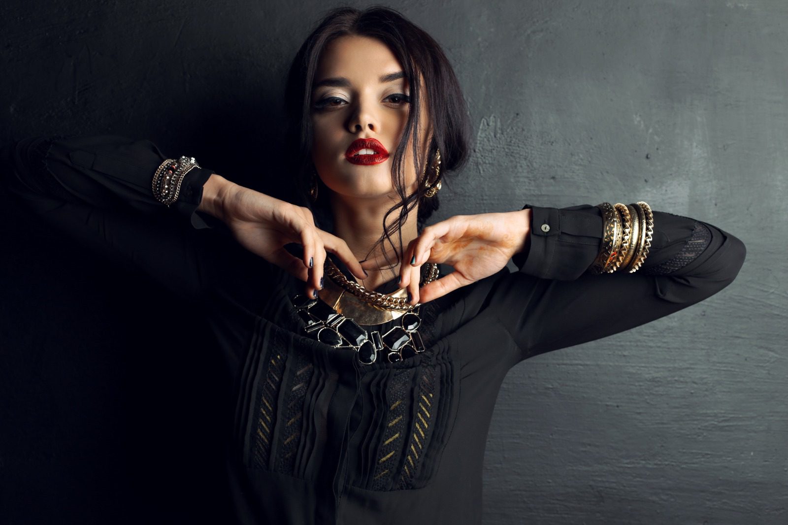 A woman with long hair and red lipstick is holding her hands up to the side of her face.