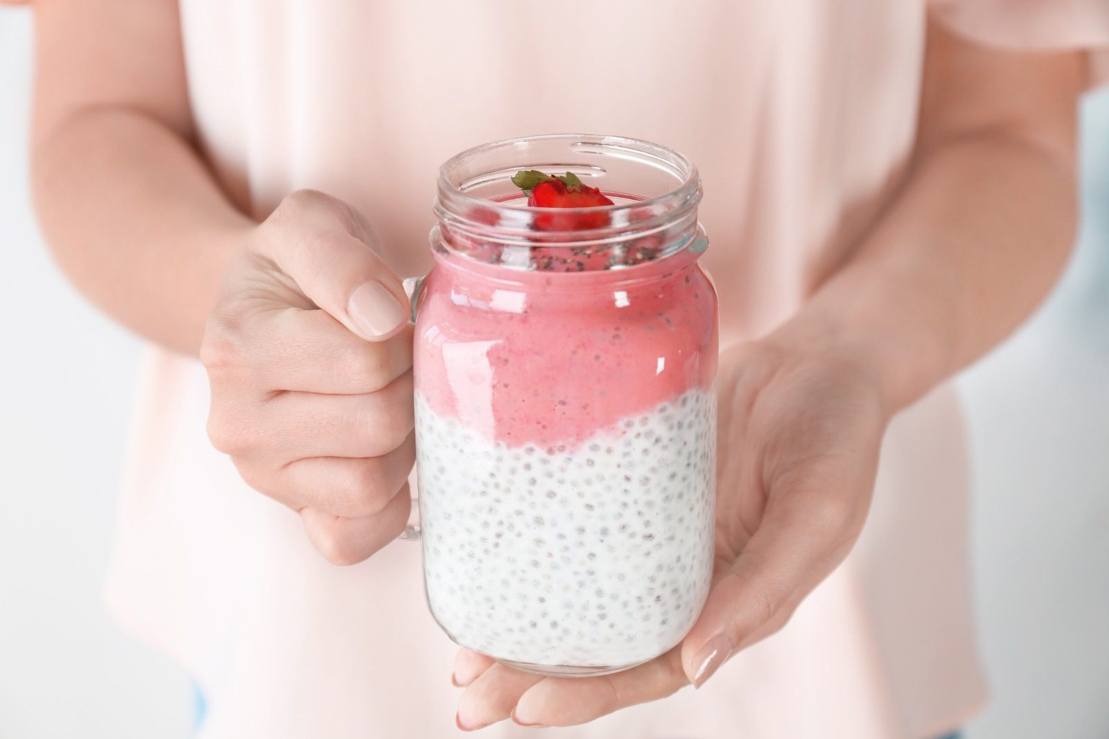 A person holding a jar of food with pink and white toppings.