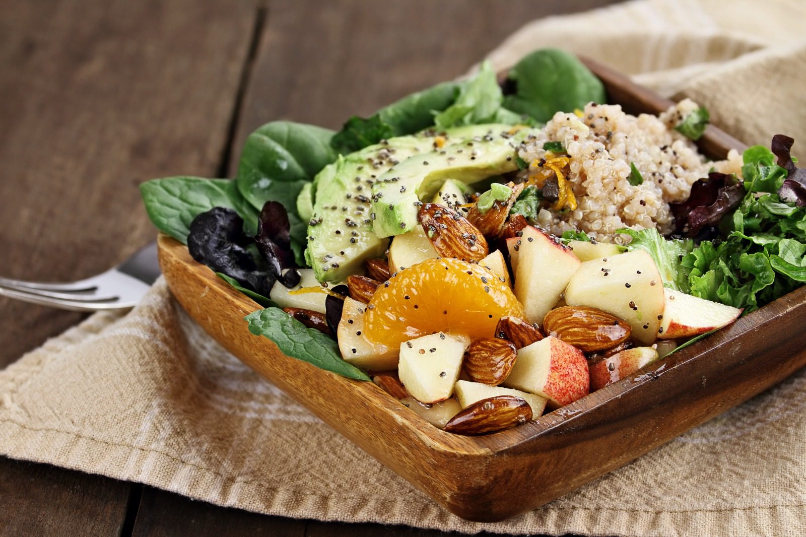 A wooden bowl filled with fruit and nuts.