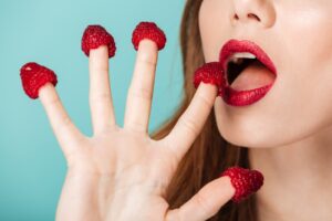 A woman with red lipstick and fingers covered in strawberries.