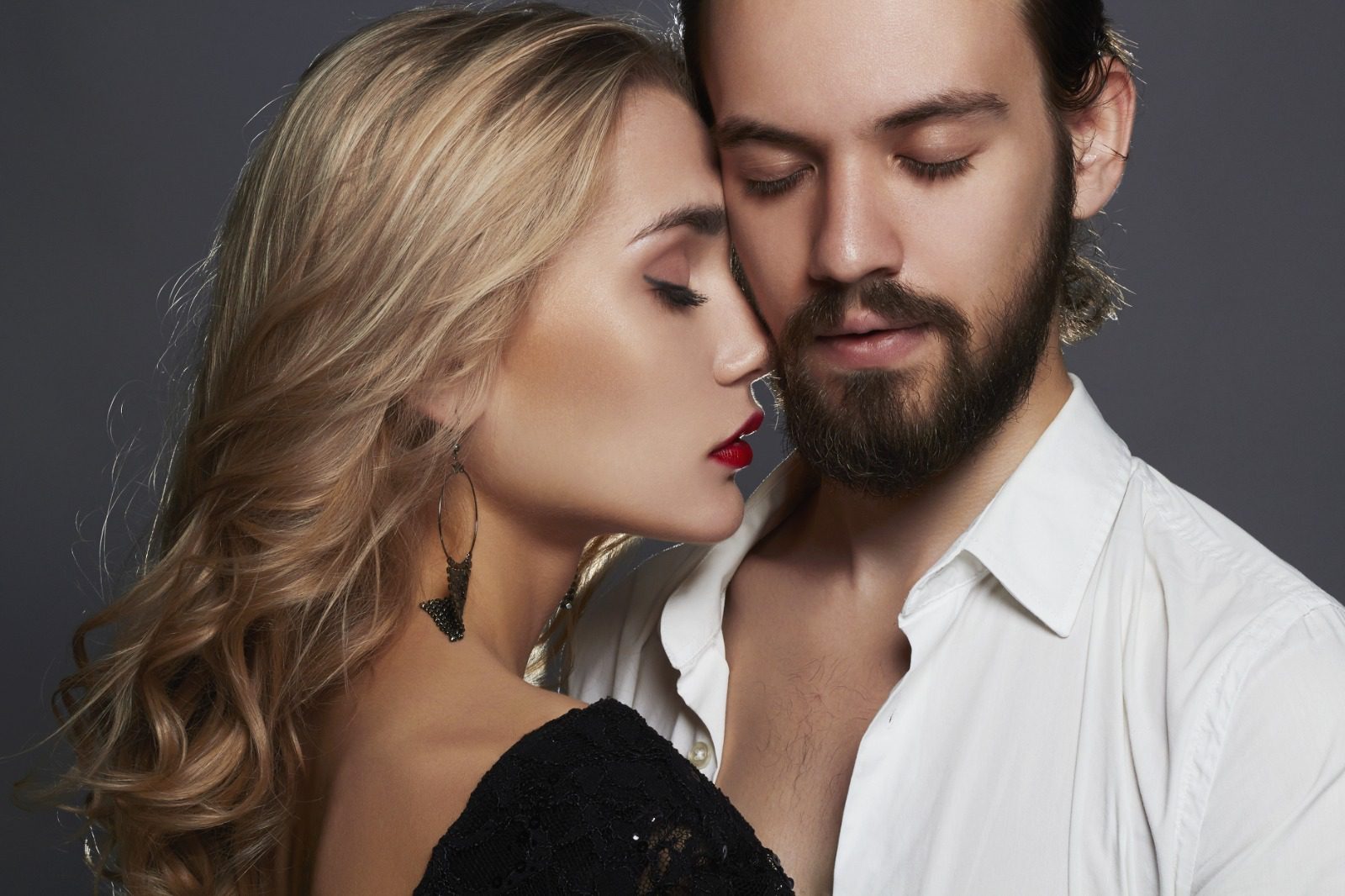 A man and woman kissing in front of a gray background.