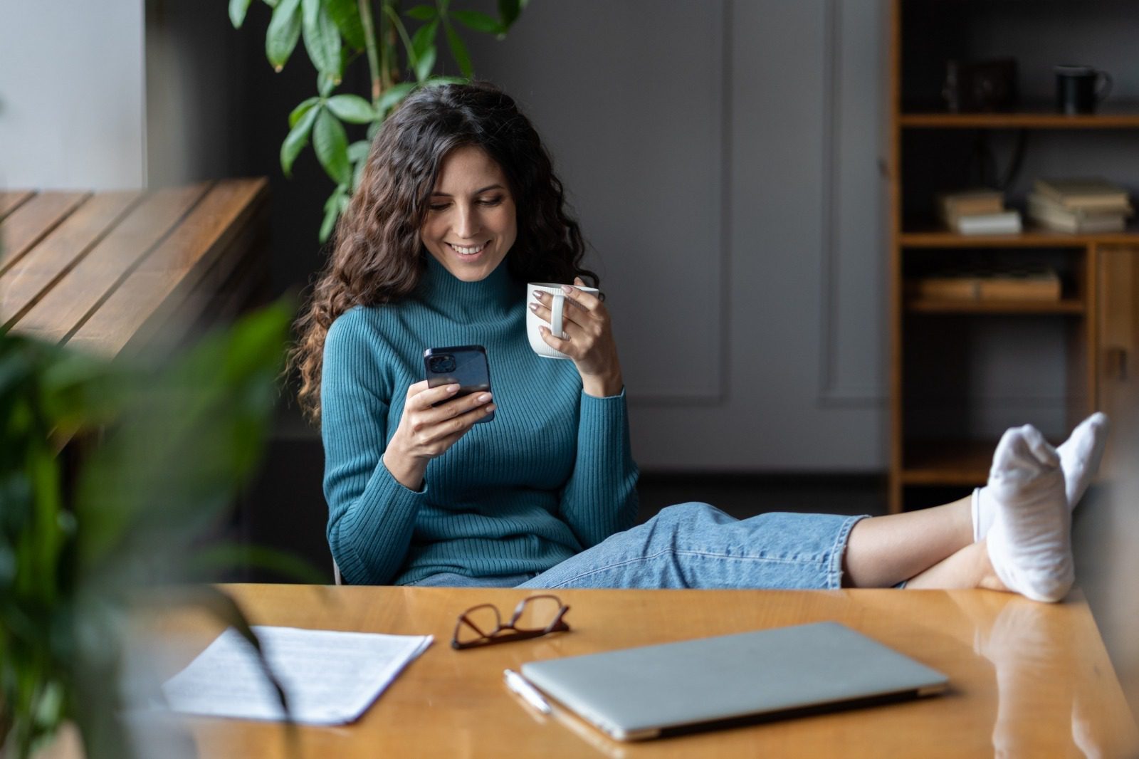 A woman sitting on the ground holding a phone and drinking coffee.